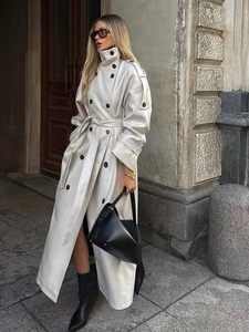 Detail of cream long trench coat featuring double-breasted buttons and waist tie belt