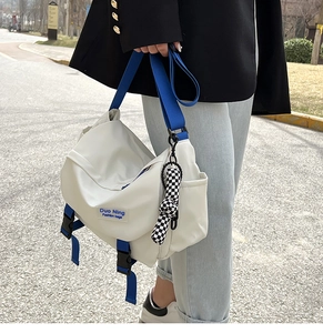 Close-up of a white nylon messenger bag with blue adjustable strap and checkered charm