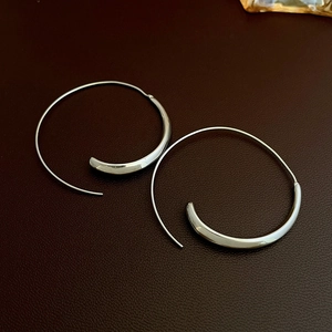 Detail view of silver geometric hoop earrings on textured dark leather background