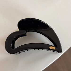 Detail view of a black heart-shaped hair claw clip with a gold 'Love' metal tag