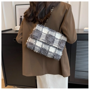 Detail of grey checkered crossbody bag with silver metal chain on model's shoulder