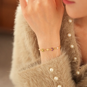Bracelet vintage doré avec des pendentifs fleurs en émail coloré sur une manche beige douce