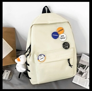 Detail view of off-white canvas backpack with cute decorative badges and plush duck pendant