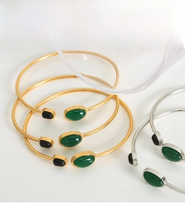 Detail of stacked gold and silver bangles with green and black gemstones on wood