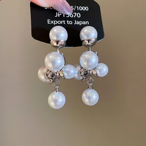 Eleganti orecchini pendenti con perle argentate e fiocco metallico su cartoncino nero