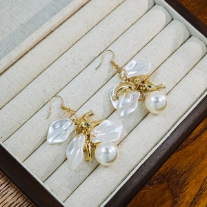 Detail of white petal pearl earrings featuring golden dolphin pendants in a jewelry box