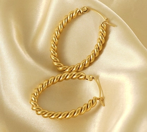 Detail of gold oval twisted hoop earrings on champagne silk background texture