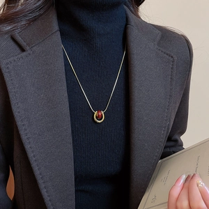 Detail of gold U-shaped pendant necklace with red stone on a black sweater