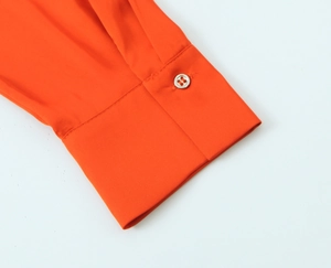Detailed close-up of single button cuff on an orange long-sleeve satin texture blouse