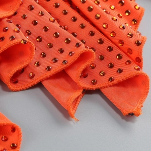 Détail du tissu côtelé orange avec strass brillants et design froncé de la robe