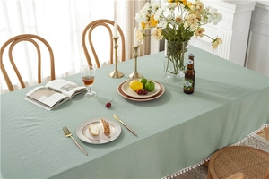 Close-up of light green cotton tablecloth with white pom-pom fringe in a cozy setting