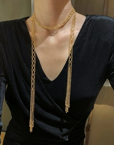 Detailed close-up of a long golden mesh tassel necklace worn over a black V-neck top
