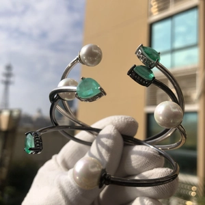 Macro detail of silver open bracelet with green pear-shaped gem and round white pearl