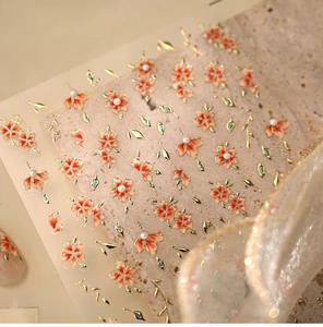 Detailed macro view of floral nail stickers with orange petals and gold accents