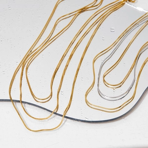 Collana minimalista a maglia serpente oro e argento su superficie a specchio bagnata
