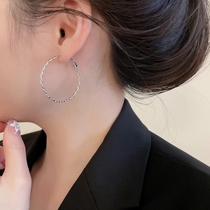 Gros plan d'une grande créole torsadée en argent sur un mannequin en costume noir