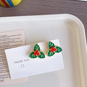 Détail de boucles d'oreilles houx de Noël avec feuilles vertes et baies rouges sur carte