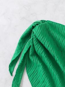Close-up of bright green eyelet fabric with wave texture and knot detail on marble