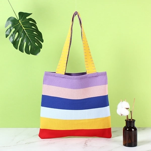 Rainbow striped knit shoulder bag for women on marble surface with green leaf background