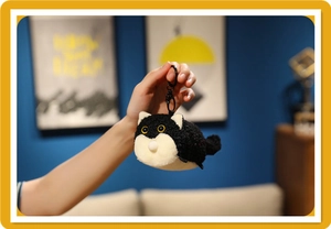 Close-up of cute black and white plush cat keychain with yellow eyes and metal ring