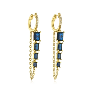Detail of gold dangle earrings featuring blue baguette stones and delicate long tassels