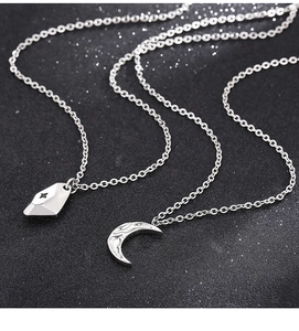 Detailed shot of crescent moon and geometric pendants on silver chains over black background