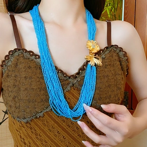 Detail of blue multi-layer beaded necklace with gold butterfly flower clasp on model