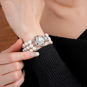Detailed close-up of multilayer pearl bracelet with rhinestone floral clasp on wrist