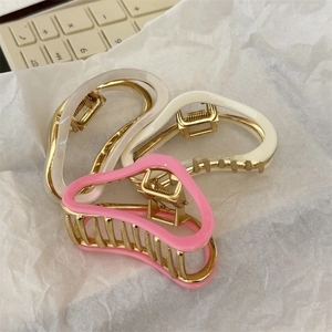 Close-up of curved acetate hair claws with gold metal frames in pink, cream and frost