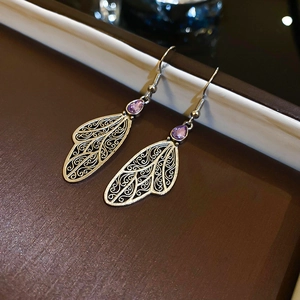 Macro shot of silver hollow-out wing earrings with purple teardrop-shaped gemstones