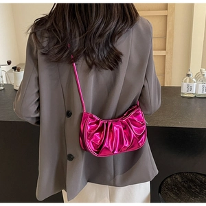 Close-up of a metallic rose pink pleated cloud bag worn over a grey blazer