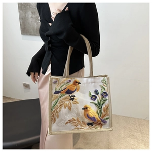 Detail of embroidered birds and flowers on a cotton linen tote bag held by a model