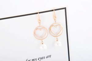 Detail of rose gold hollow circle earrings with heart motif and white pearl drops