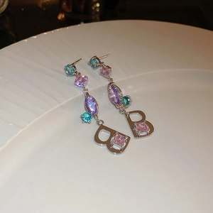 Detailed shot of long silver earrings with colorful zircons and a letter B pendant