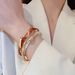 Detail of gold-plated wavy bangles with amber and pearl white resin accents on a model