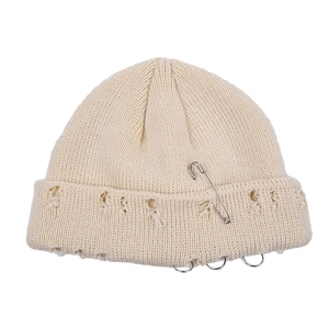 Detail of distressed beige beanie with safety pin and silver metal rings trim