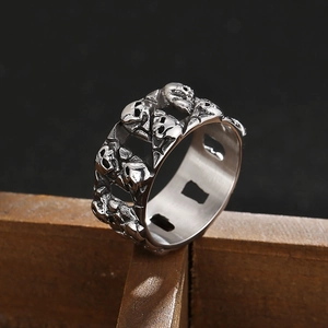 Macro detail of silver punk skull chain ring with relief carving on a dark wooden base