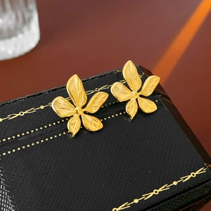 Close-up of gold flower earrings featuring brushed metal petals on black leather box