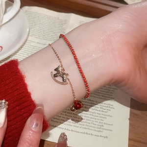 Detail of a layered gold-plated bracelet with red gemstones and a diamond horse charm
