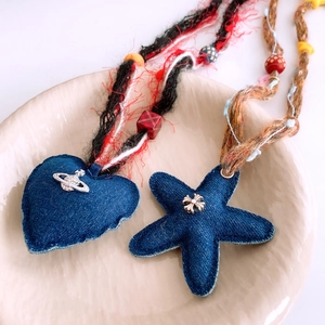 Dettagli macro dei ciondoli a cuore e stella in denim con perle e corde intrecciate