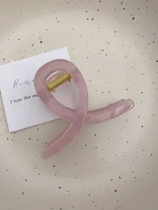 Détail d'une pince à cheveux rose poudré translucide avec ressort doré sur plateau
