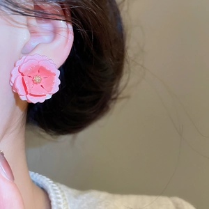 Gros plan d'une boucle d'oreille fleur en résine rose portée sur l'oreille d'un mannequin