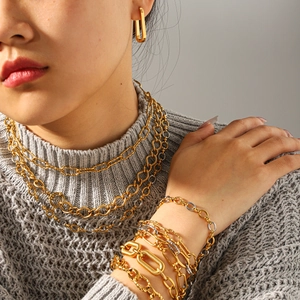 Primo piano di collane e bracciali a catena sovrapposti in oro e argento su una modella