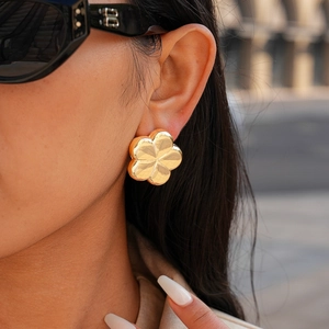 Close-up of model wearing large gold-finished flower earrings with polished wavy petals