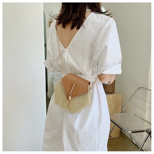 Detail of woven straw crossbody bag with brown flap and gold chain strap on model