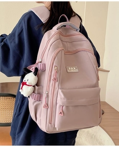 Pink nylon backpack detail with multi-pocket design and cute white puppy plush charm