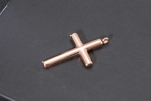 Close-up of polished rose gold cross pendant on a dark textured surface background