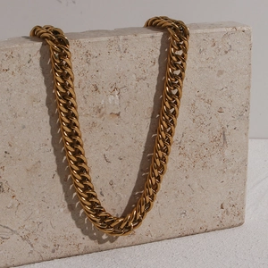 Detail of chunky gold Cuban link necklace with OT buckle on a textured stone block