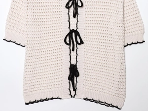 Macro view of beige crochet knit polo top with black bow ties and scalloped edges