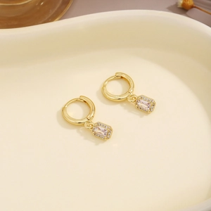 Detail view of gold earrings featuring a rectangular crystal drop with small diamonds